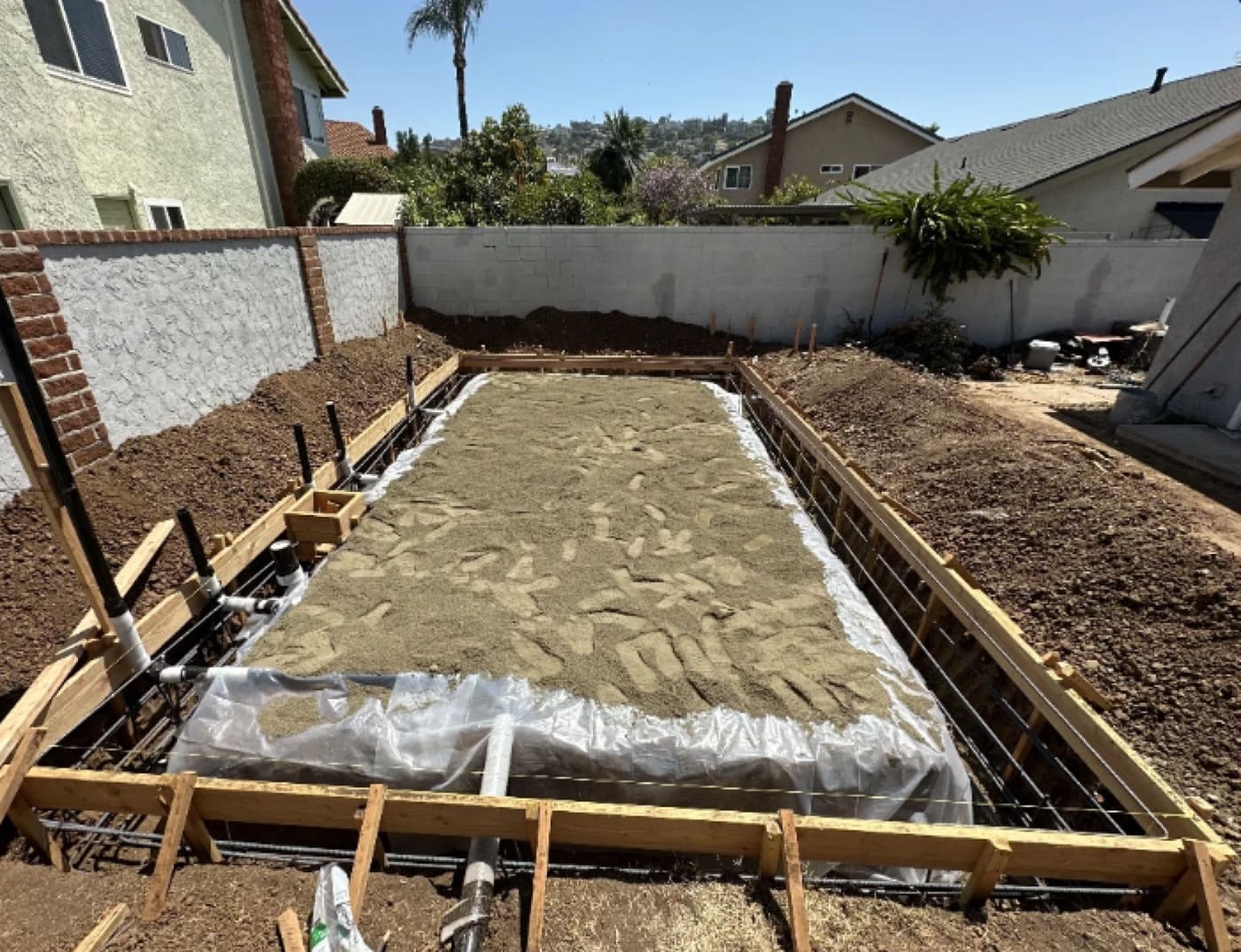 Sand bed and vapor barrier over rebar with capped plumbing stubs, ready for the ADU slab pour