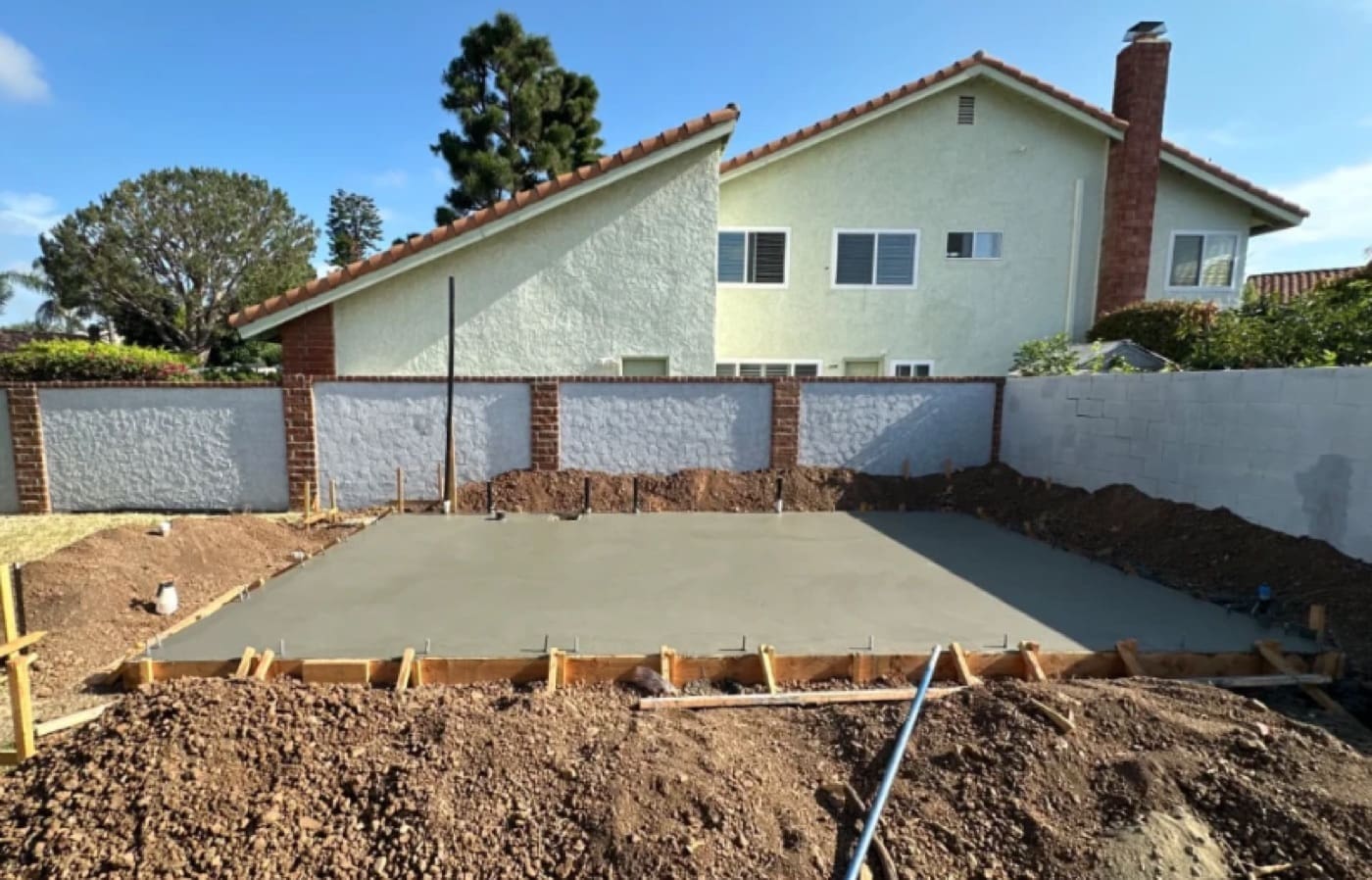 Completed ADU slab with plumbing stub-ups and the main house in the background