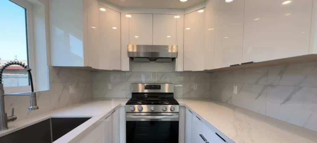 Two-story ADU kitchen with European flat high-gloss white cabinets, quartz counters, stainless steel range and marble-look backsplash